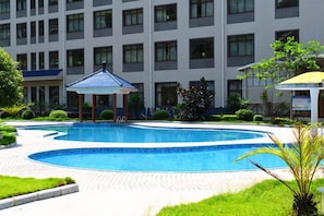 Une piscine agrémentée d’un belvédère, entourée d’une pelouse bien entretenue et d’un bâtiment doté de nombreuses fenêtres.