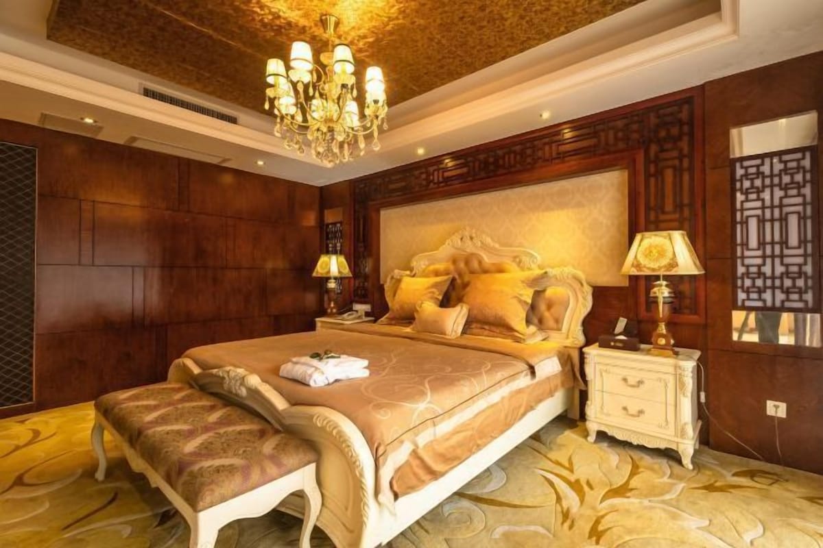Un dormitorio amplio con una cama grande, un cabecero decorado y una araña.