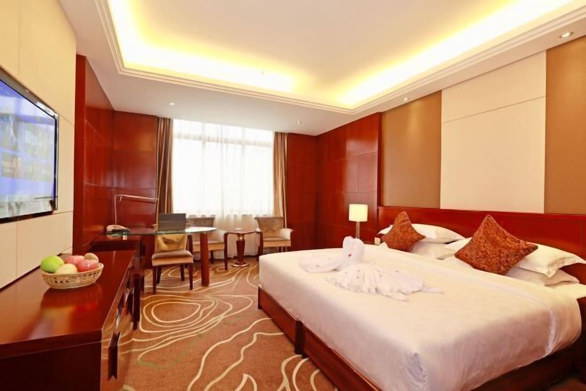 Una habitación de hotel con una cama grande, un escritorio con una silla, un televisor y una zona de comedor con mesa y sillas.