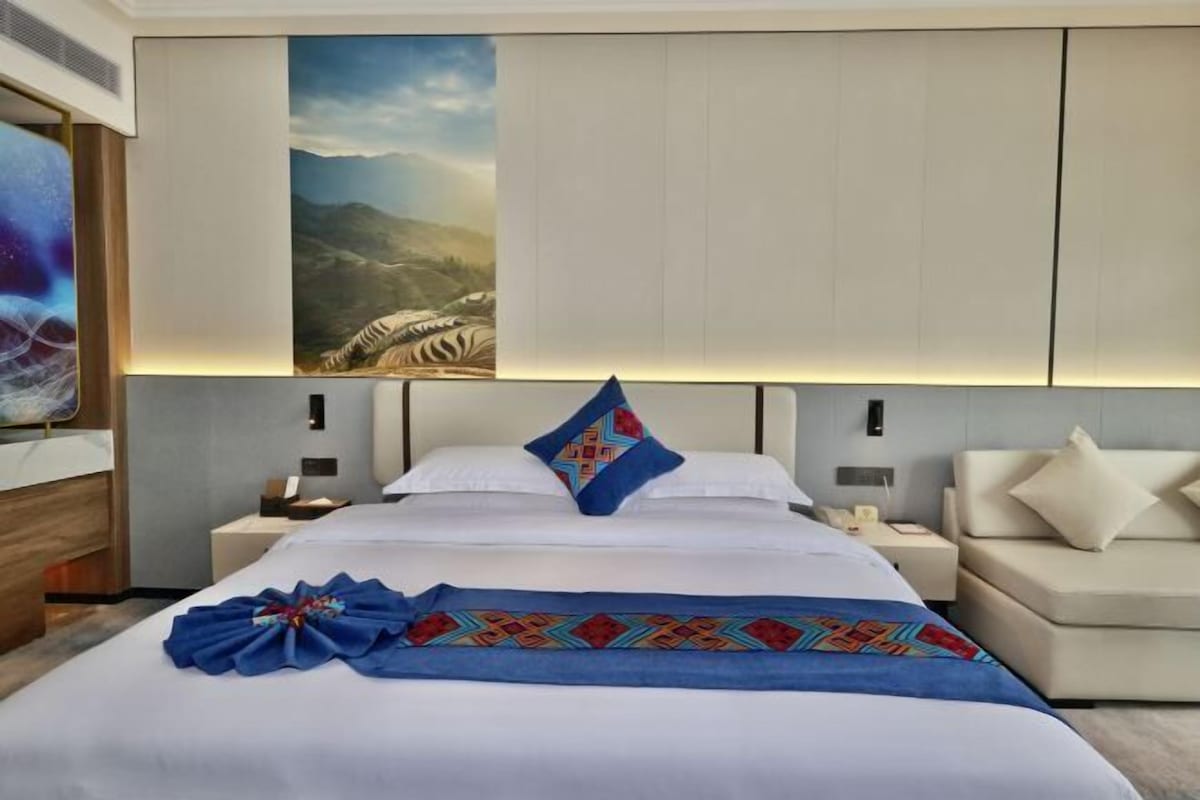 Una habitación de hotel moderna con una cama grande, una mesita de noche, un sofá y un televisor montado en la pared.