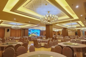 A banquet hall with round tables, chairs, chandeliers, and a large screen.