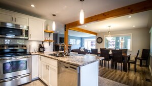 Una cocina moderna con electrodomésticos de acero inoxidable, lavavajillas y un comedor con sillas y mesa de madera.