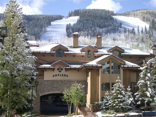 A lodge named 'Antlers' with a stone arch entrance, multiple chimneys, and a view of a snowy mountain in the background.