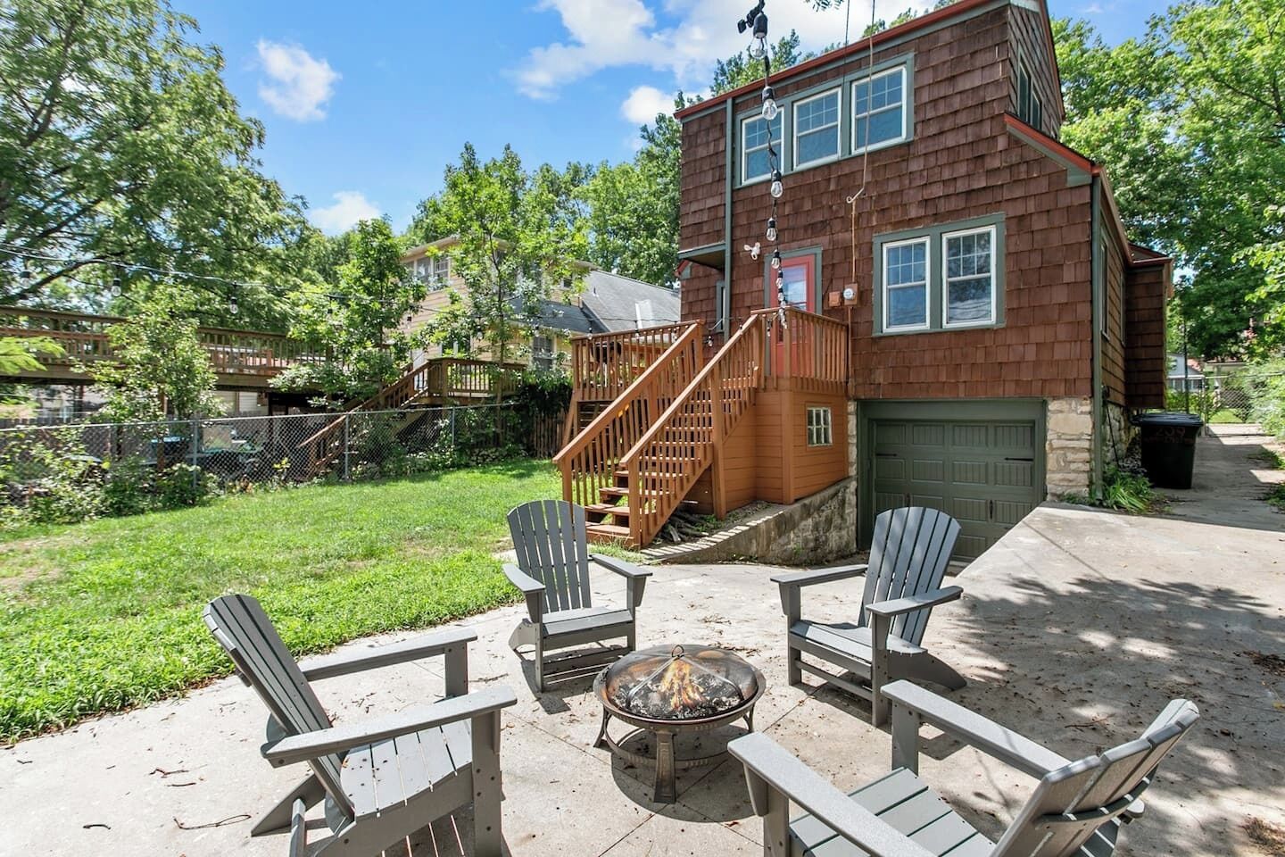 A backyard with a fire pit, wooden deck, and Adirondack chairs.