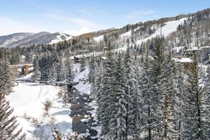 A snow-covered mountain landscape with a river, a bridge, and buildings in the background.