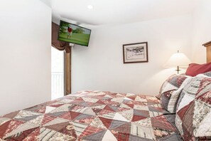 A hotel room with a bed, a flat-screen TV mounted on the wall, a framed picture, and a bedside lamp.