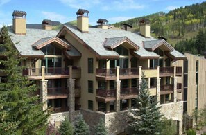 A multi-story hotel with balconies, large windows, and a mountainous backdrop.