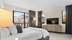 Ett modernt hotellrum med en stor säng, en platt-TV, en byrå och utsikt över ett bergigt landskap.