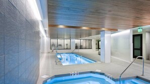 Ett inomhusbadområde med två pooler, ett träbeklätt tak och en modern design.
