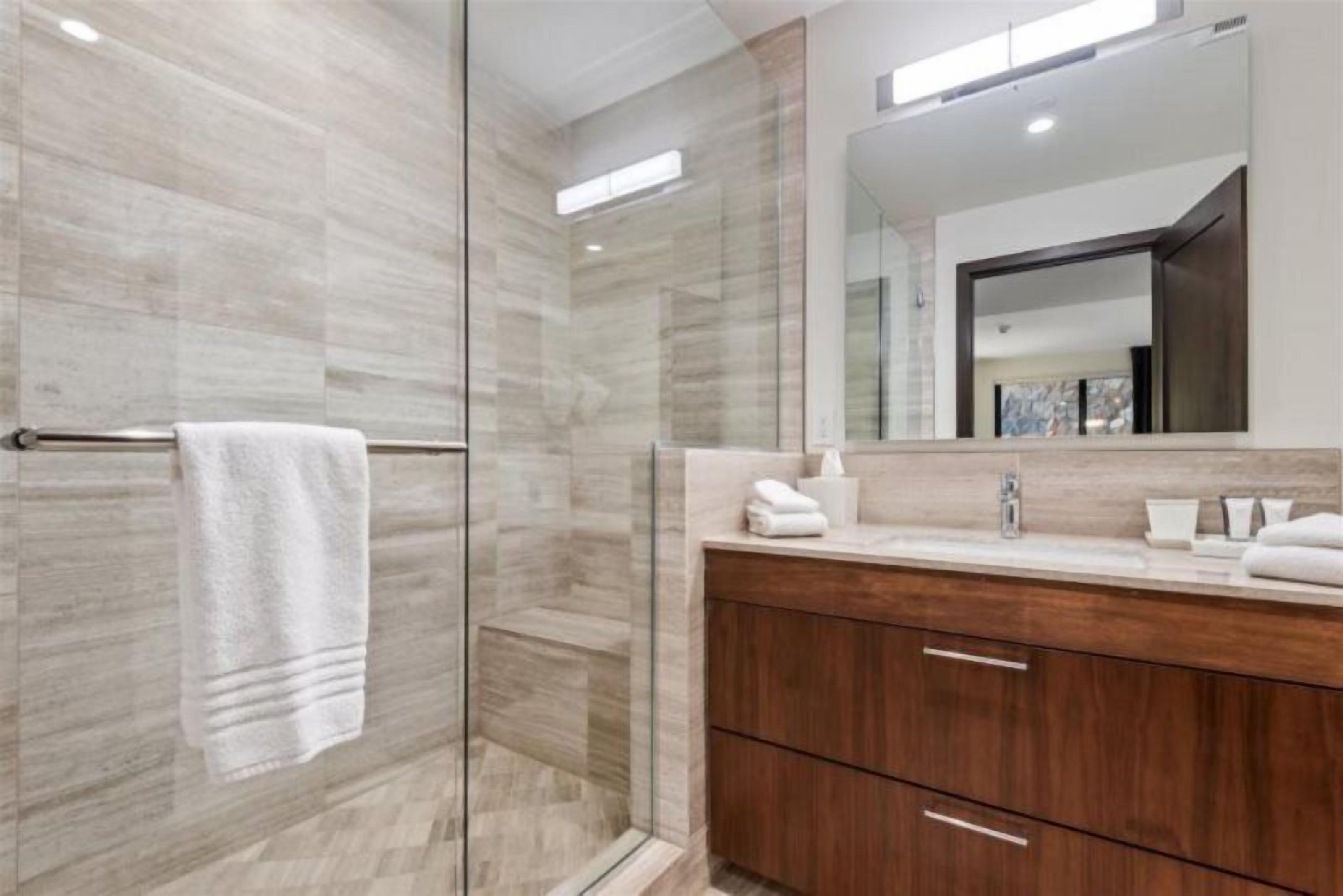 A modern bathroom with a glass shower enclosure, a wooden vanity with a mirror, and a towel rack.