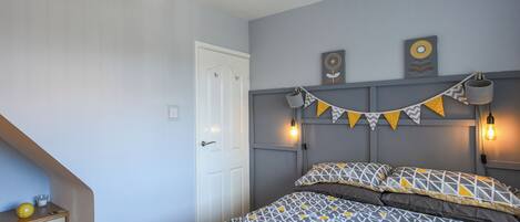 A bedroom with a bed, a dresser, a door, and wall-mounted lights.
