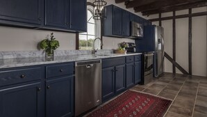 A modern kitchen with dark blue cabinets, stainless steel appliances, and a marble countertop. - Comissary Middleburg (Huger)