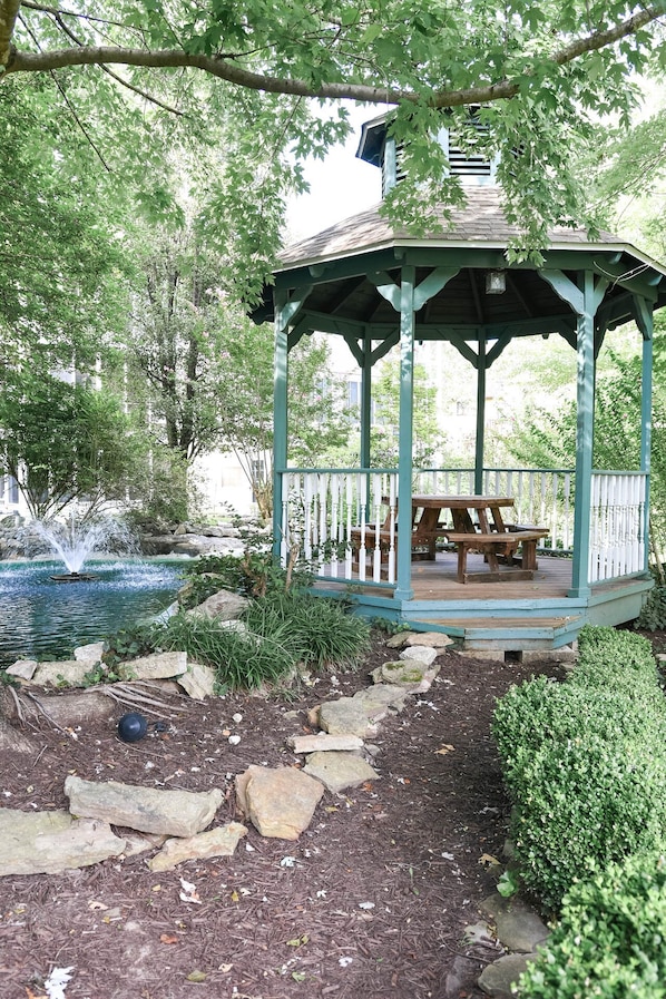 A gazebo with a picnic table, surrounded by a pond and rocks.