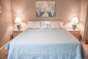 A bedroom with a large bed, two bedside lamps, and a painting on the wall.