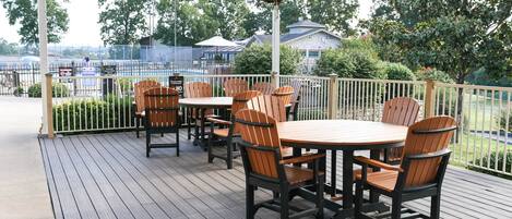 Un patio al aire libre con terraza de madera, mesas redondas y sillas tipo Adirondack.