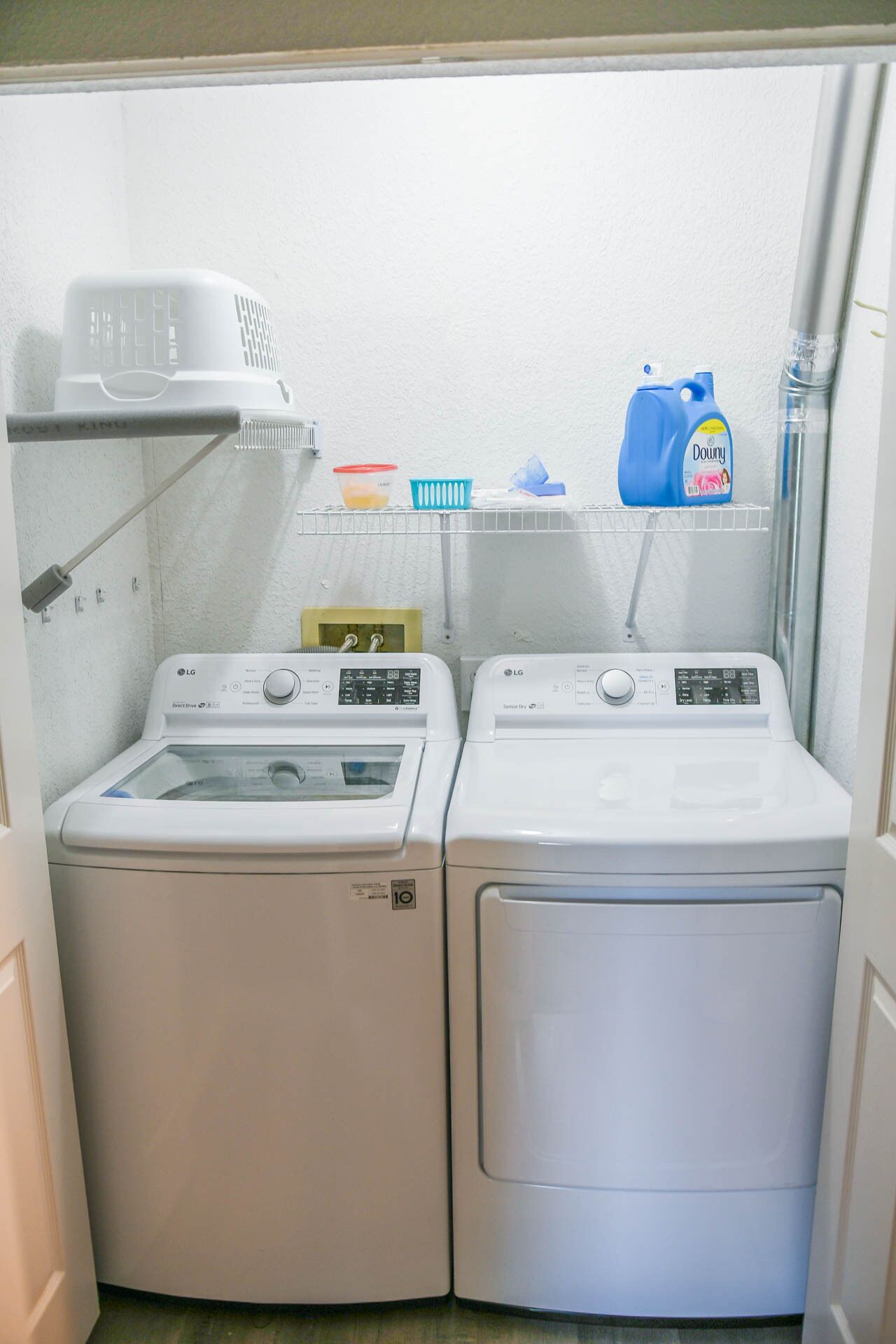 A laundry area with two white LG washing machines, a shelf with laundry supplies, and a white wall.