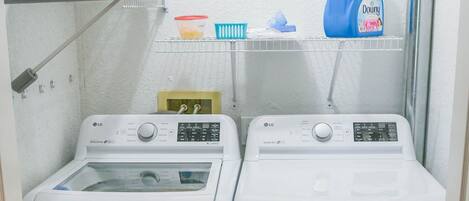 A laundry area with two white LG washing machines, a shelf with laundry supplies, and a white wall.
