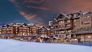A multi-story lodge with a snow-covered ground, featuring a mix of wooden and stone architecture, and multiple balconies.