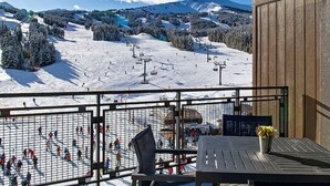 A balcony with a view of a snowy ski slope, a table, and chairs.