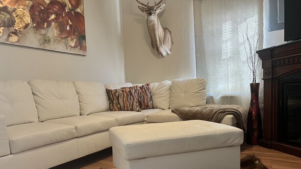 Un salon avec un canapé d’angle blanc, une tête de cerf décorative, un tableau et un tapis en fourrure sur le sol.