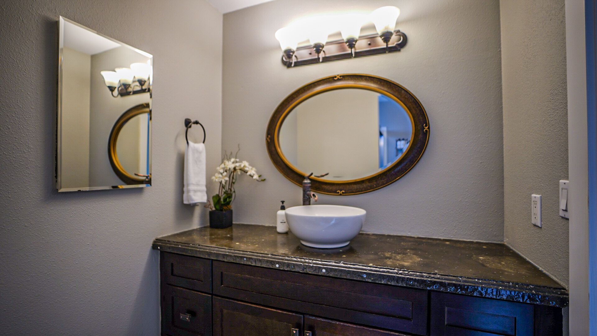 Une salle de bain avec un miroir rond, un lavabo blanc et un meuble-lavabo en bois foncé.