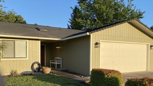 Ein eingeschossiges Haus mit Garage, einer Veranda mit Bank und einem kleinen Garten.