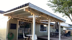 Ein überdachter Patio-Bereich mit Lichterketten, einem Tisch und Stühlen sowie Blick auf den Garten.