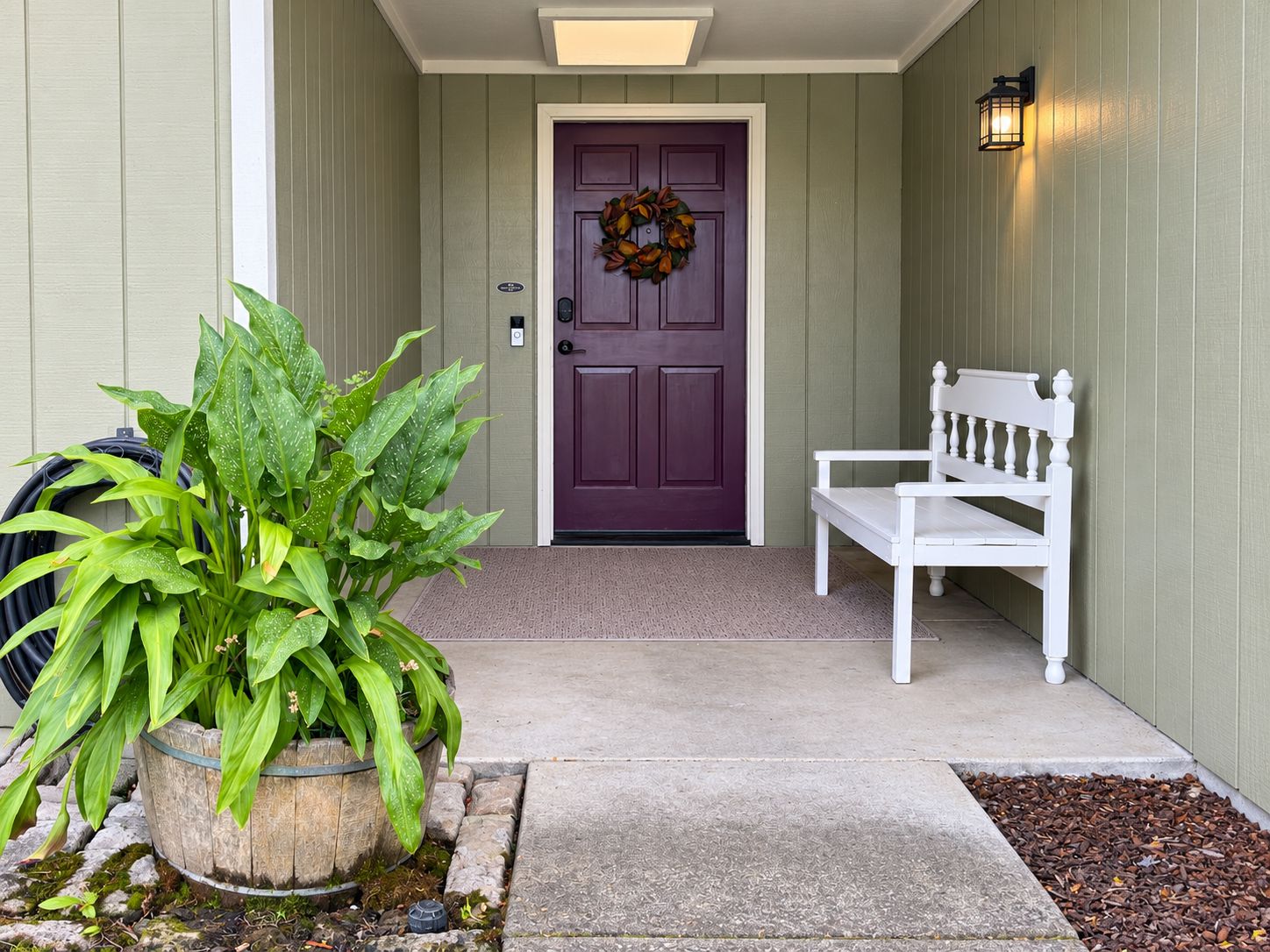 A front porch with a purple door, a white bench, and a potted plant.