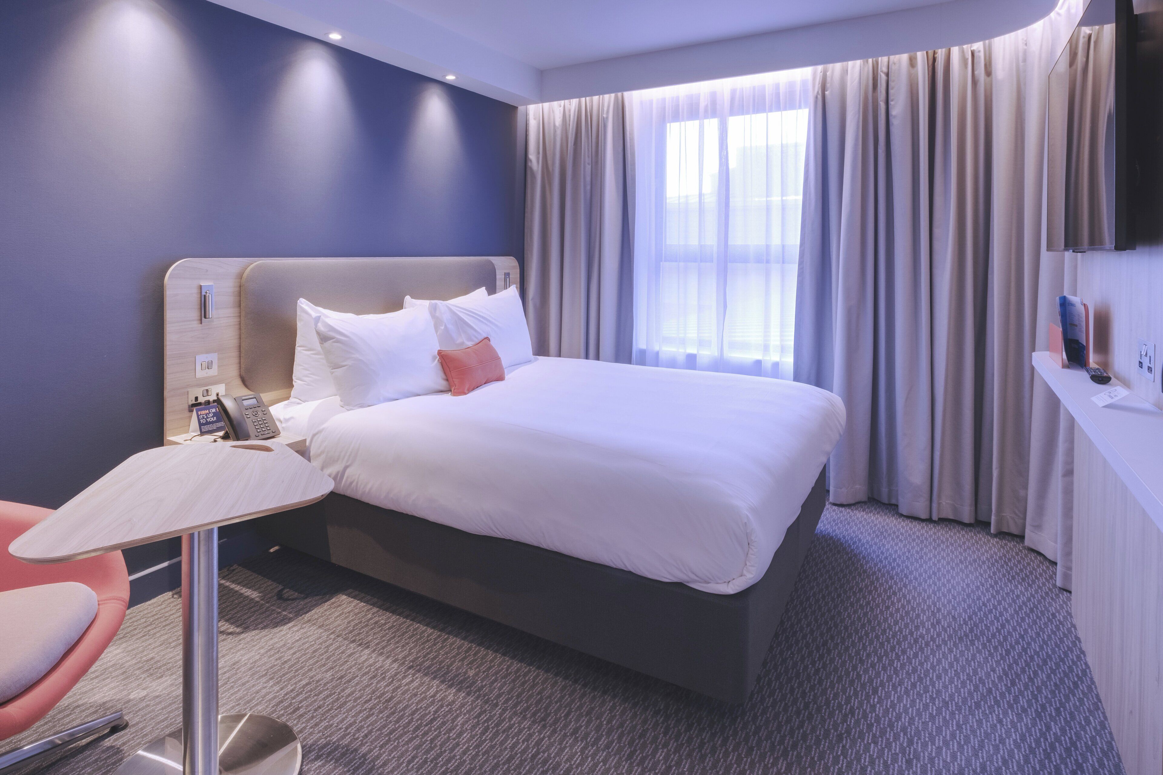 A hotel room with a bed, a desk with a telephone, and a television on the wall.