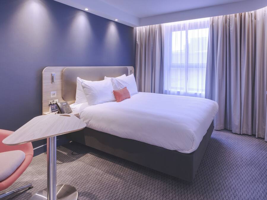 A hotel room with a bed, a desk with a telephone, and a television on the wall.