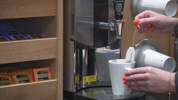 A coffee machine dispensing coffee into a cup, with a shelf of Twinings English tea bags visible.