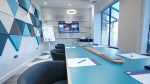 A conference room with a long table, chairs, a whiteboard, and a TV screen displaying a cityscape. - Holiday Inn Express Fleet (Fleet)