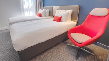 A hotel room with two beds, a red chair, and a view of the outdoors.