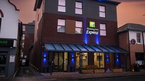 A Holiday Inn Express building with a glass storefront, brick facade, and a blue awning. - Holiday Inn Express Fleet (Fleet)