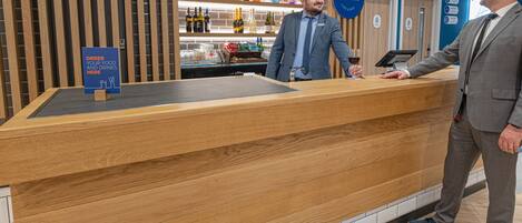 Un mostrador de recepción con detalles de madera, un cartel que indica dónde pedir comida y bebidas, y una exhibición de varias botellas al fondo.
