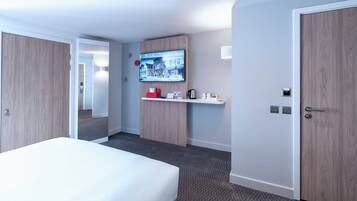 Une chambre d’hôtel avec un lit, un téléviseur fixé au mur, une petite étagère avec quelques objets et une porte.