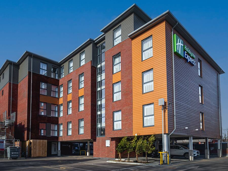 A multi-story Holiday Inn Express building with a modern design, featuring a mix of brick and wood paneling, large windows, and a parking garage.