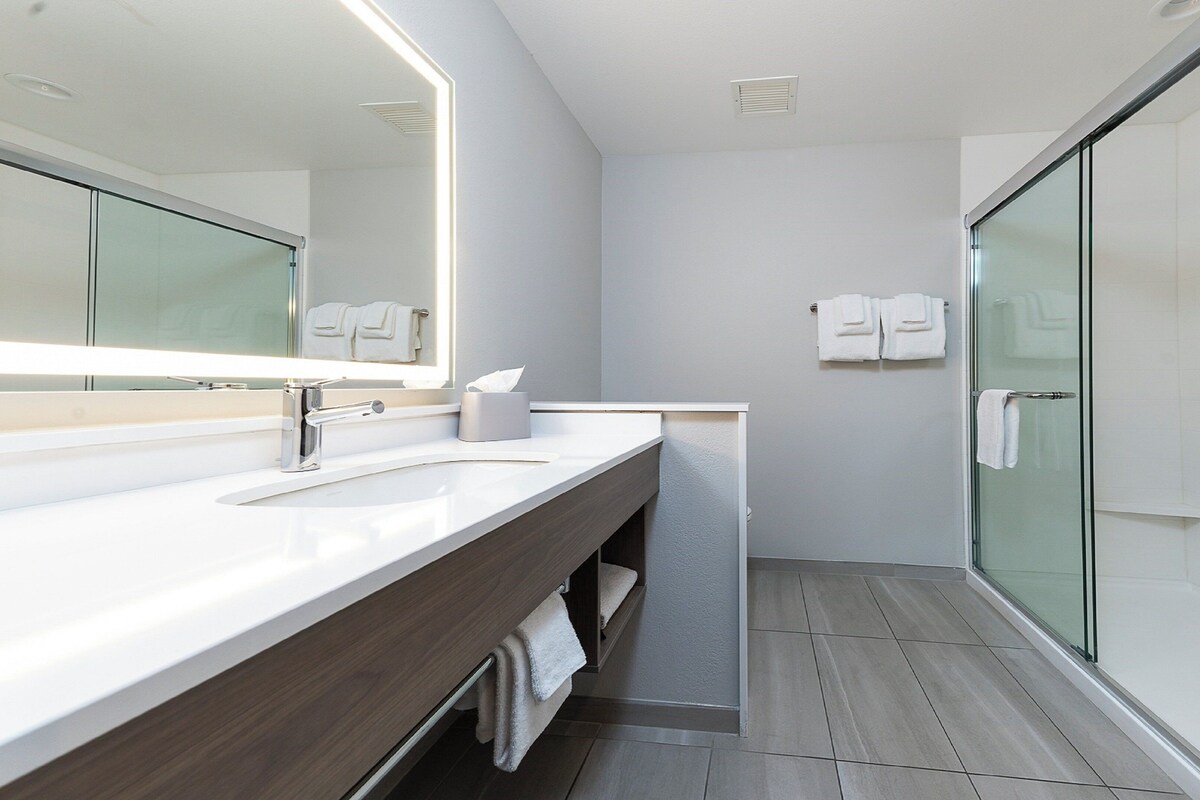 Un bagno moderno con uno specchio grande, un lavabo, box doccia in vetro e un porta asciugamani.