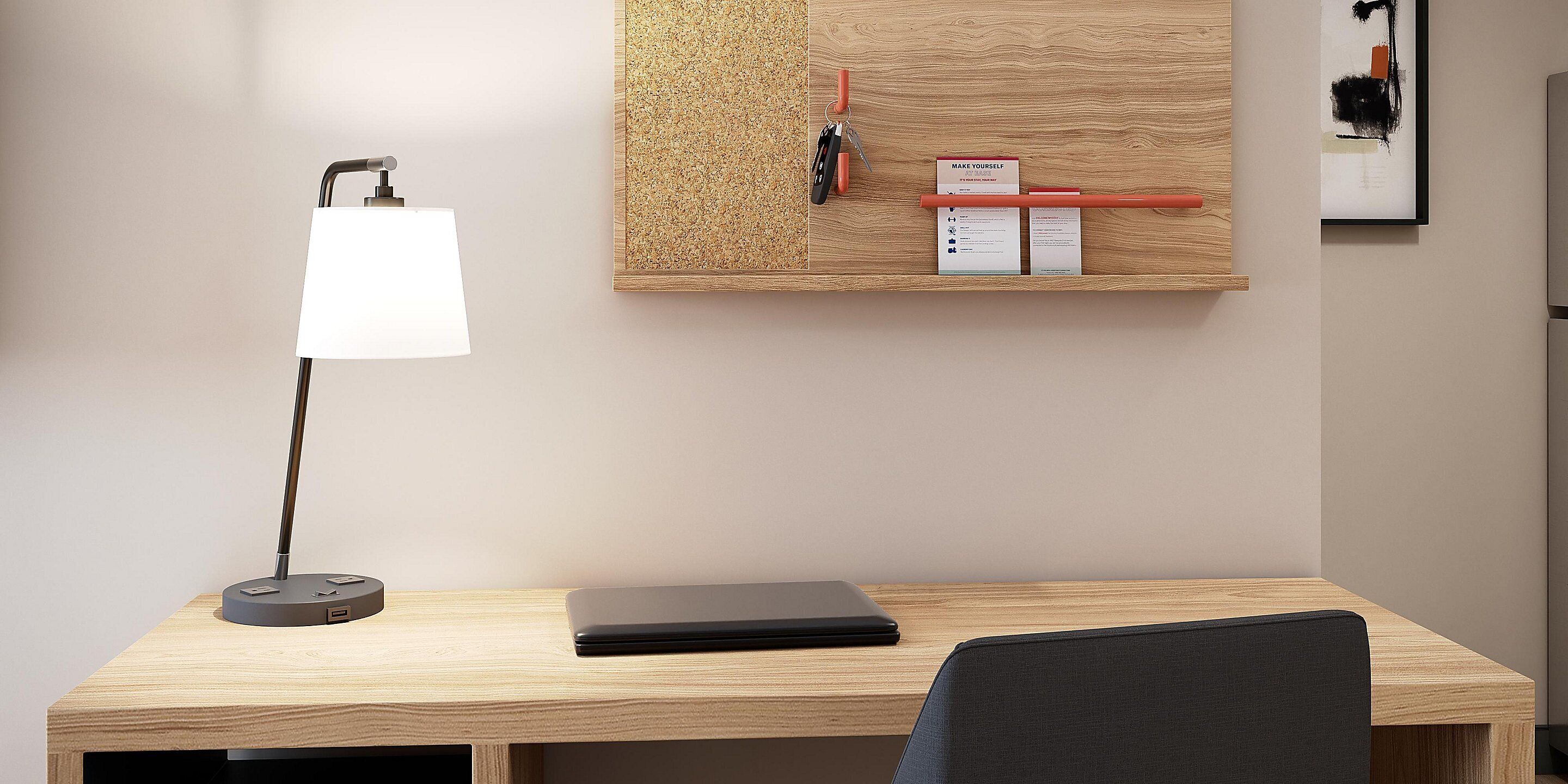 A modern office desk with a laptop, a desk lamp, and a corkboard with notes and a sign.