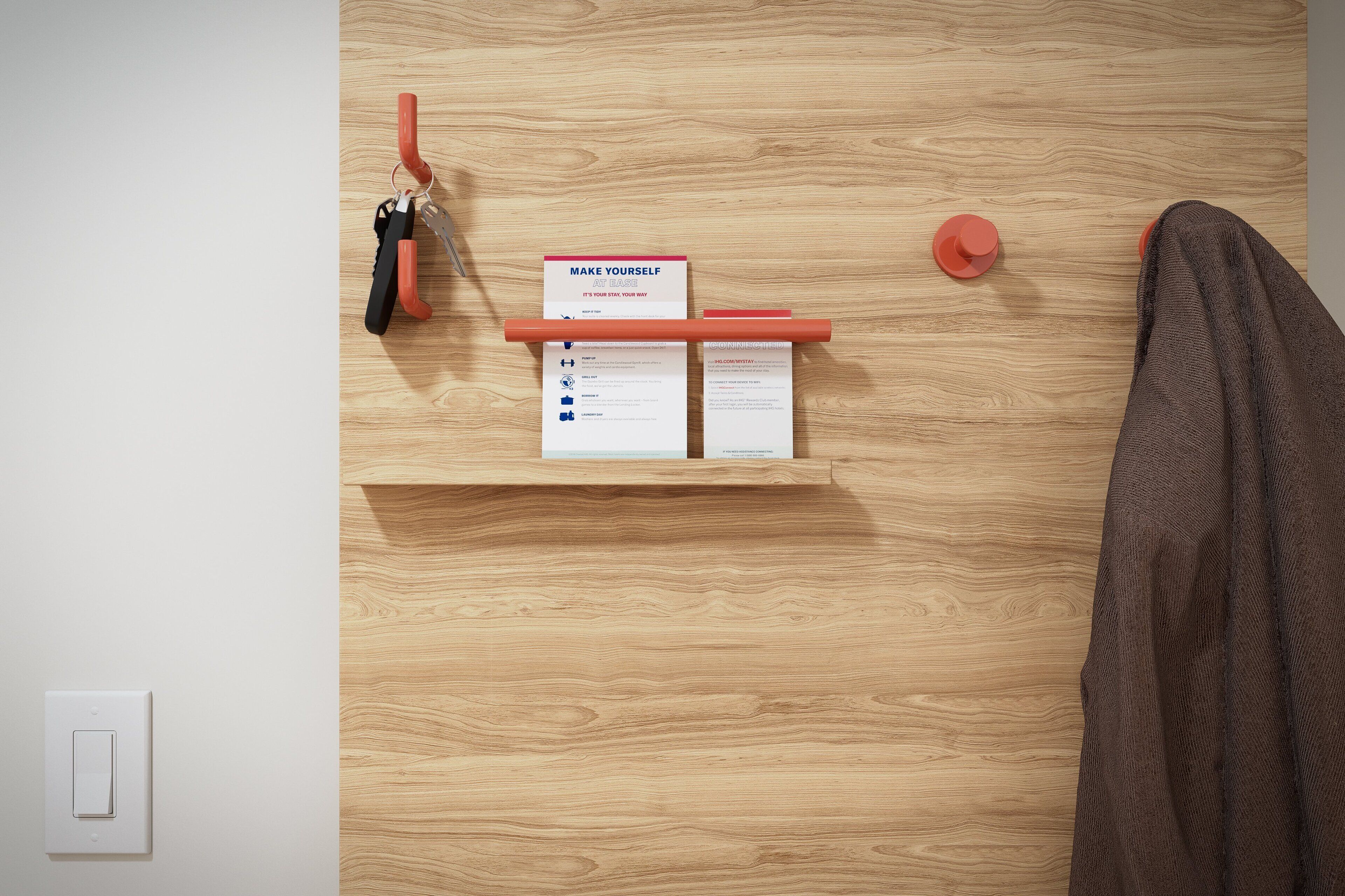 Pared de madera con un estante que sostiene un gancho rojo, un botón rojo y una tarjeta con texto motivacional.