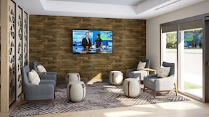 A modern living room with a large flat-screen TV mounted on a wooden wall, grey armchairs with patterned cushions, and a patterned rug.
