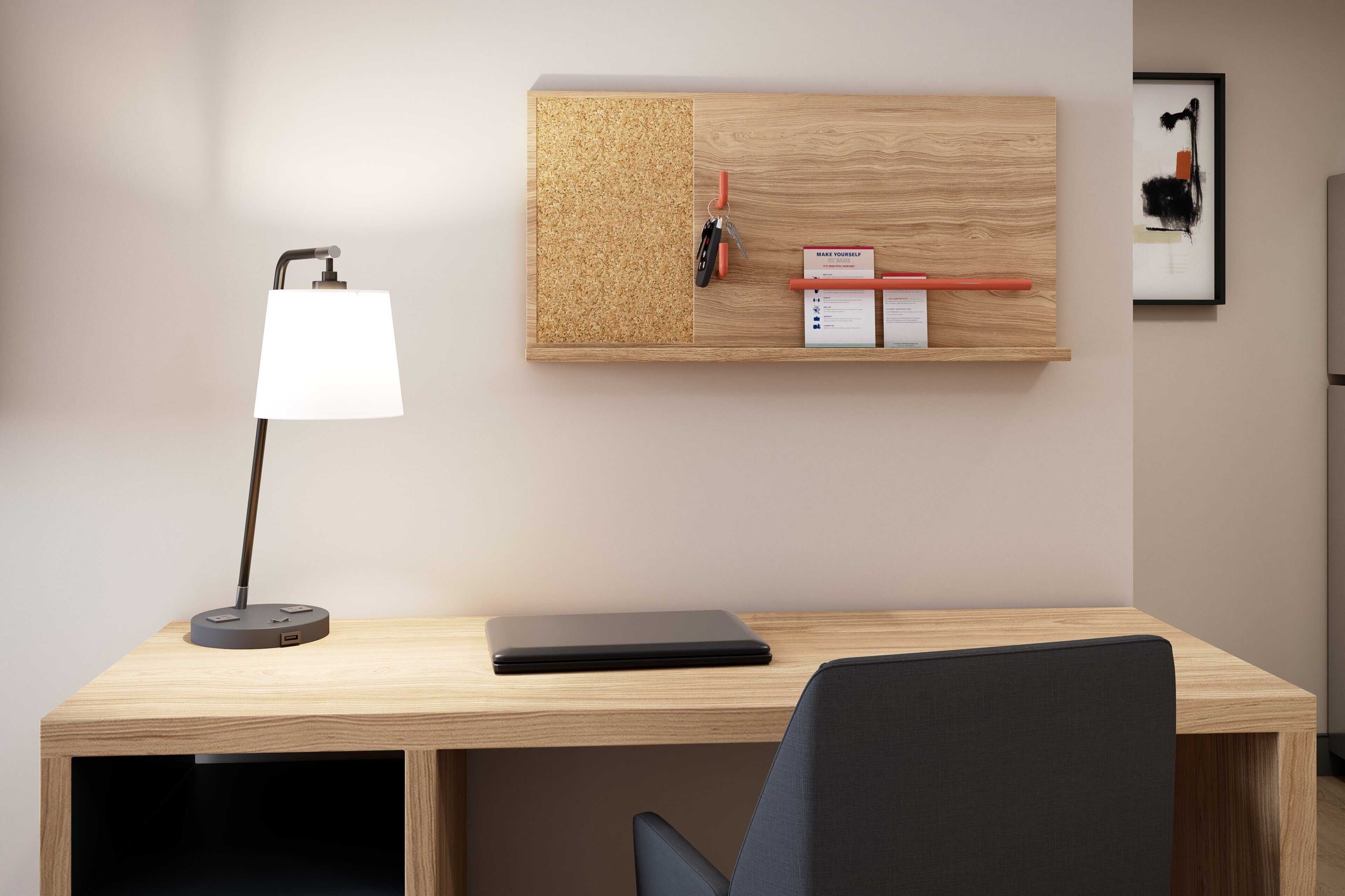 A modern office desk with a laptop, a desk lamp, and a corkboard with office supplies.