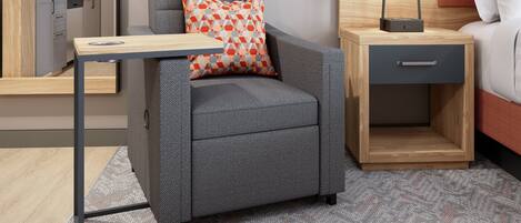 Habitación compacta con sofá gris, una pequeña mesita de madera, un cajón y una cama con cabecera.