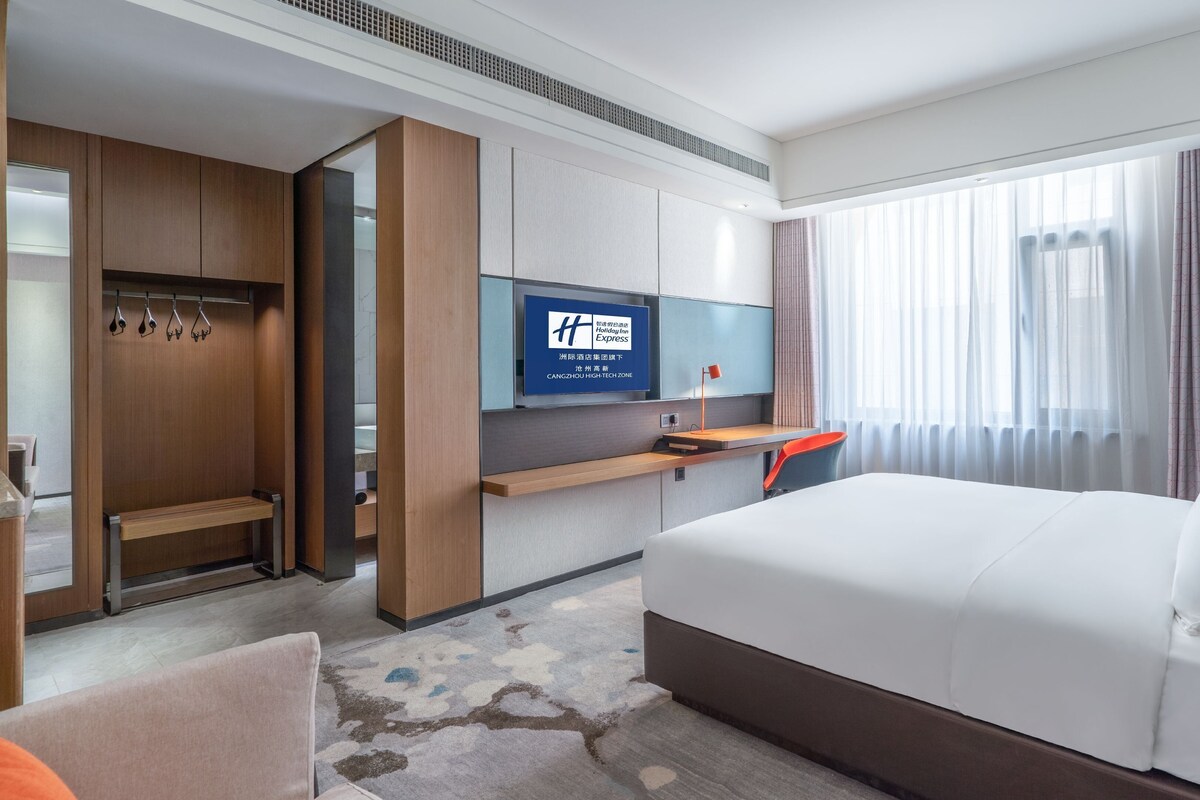 A hotel room with a bed, a desk, a TV, a wardrobe, and a bathroom.