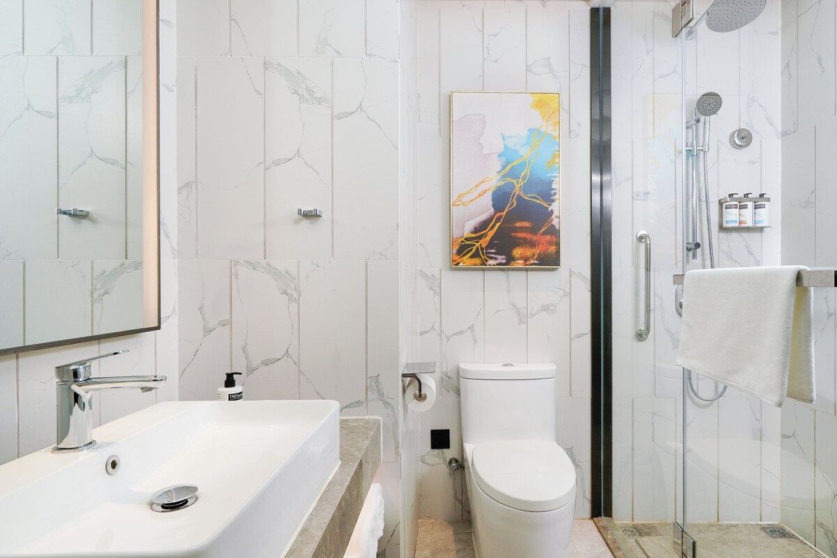 A modern bathroom with a white marble sink, a toilet, and a shower area.
