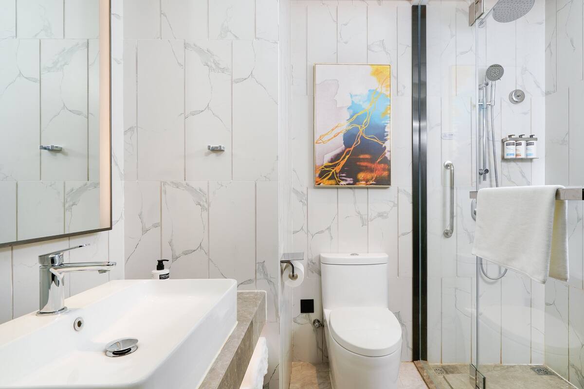 A modern bathroom with a white marble sink, a toilet, and a shower area.