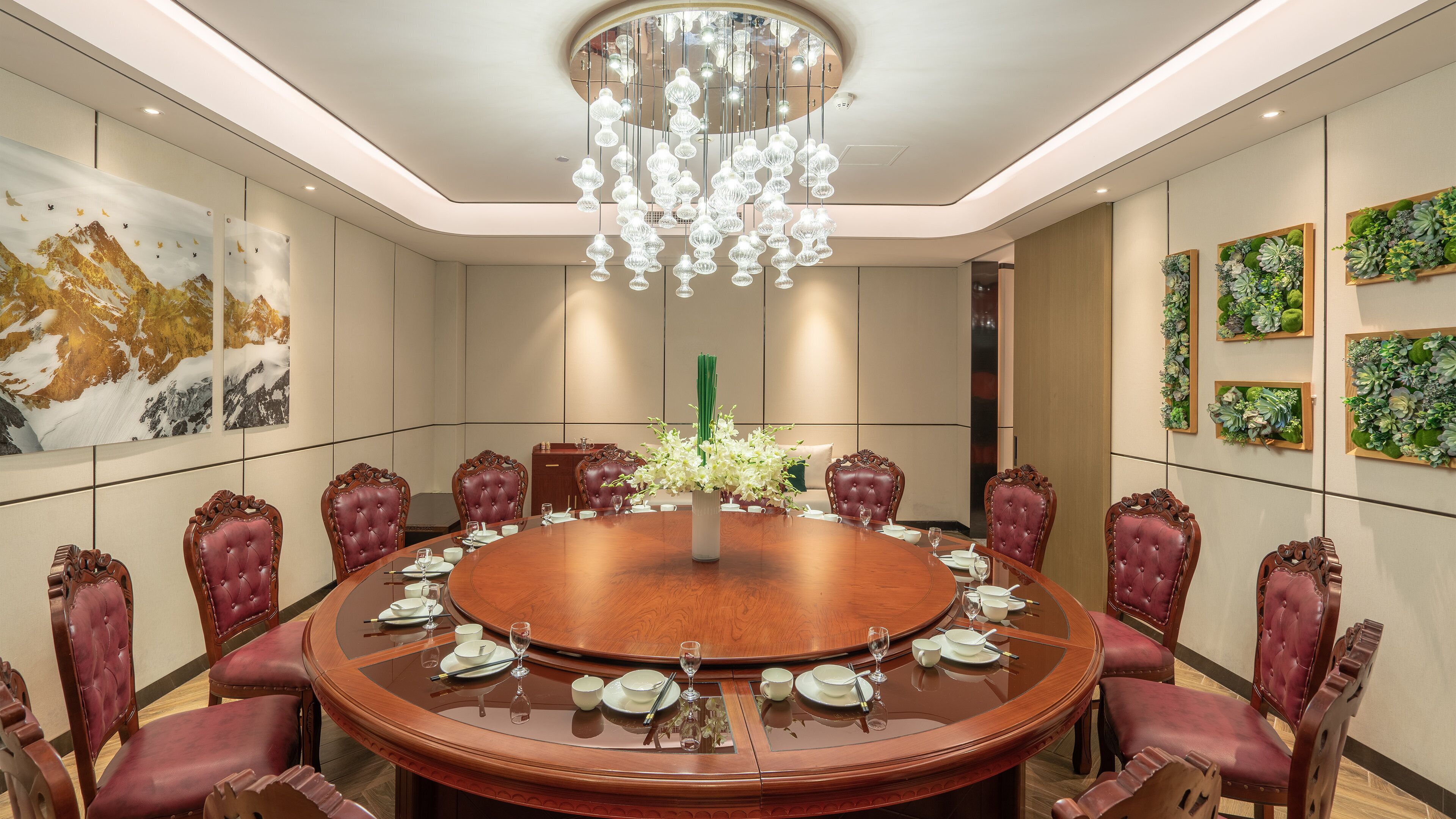 A conference room with a round table, leather chairs, a chandelier, and wall art.