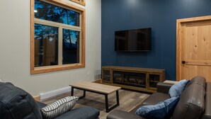 A modern living room with a fireplace, leather sofas, a TV, and a large window with a view of trees. - Red Fox Lodge, 2 bedroom, 2 bathroom with Hot Tub (Golden)