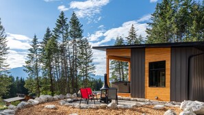 A modern cabin with a wooden exterior, a stone-paved patio, and a red chair. - Red Fox Lodge, 2 bedroom, 2 bathroom with Hot Tub (Golden)