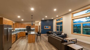 A modern kitchen with wooden cabinets, a stainless steel refrigerator, and a dining area with a sofa and tables. - Red Fox Lodge, 2 bedroom, 2 bathroom with Hot Tub (Golden)